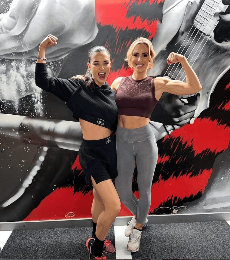 Amy Jackson and Sarah Lindsay flexing in front of the gym mural at ROAR Fitness
