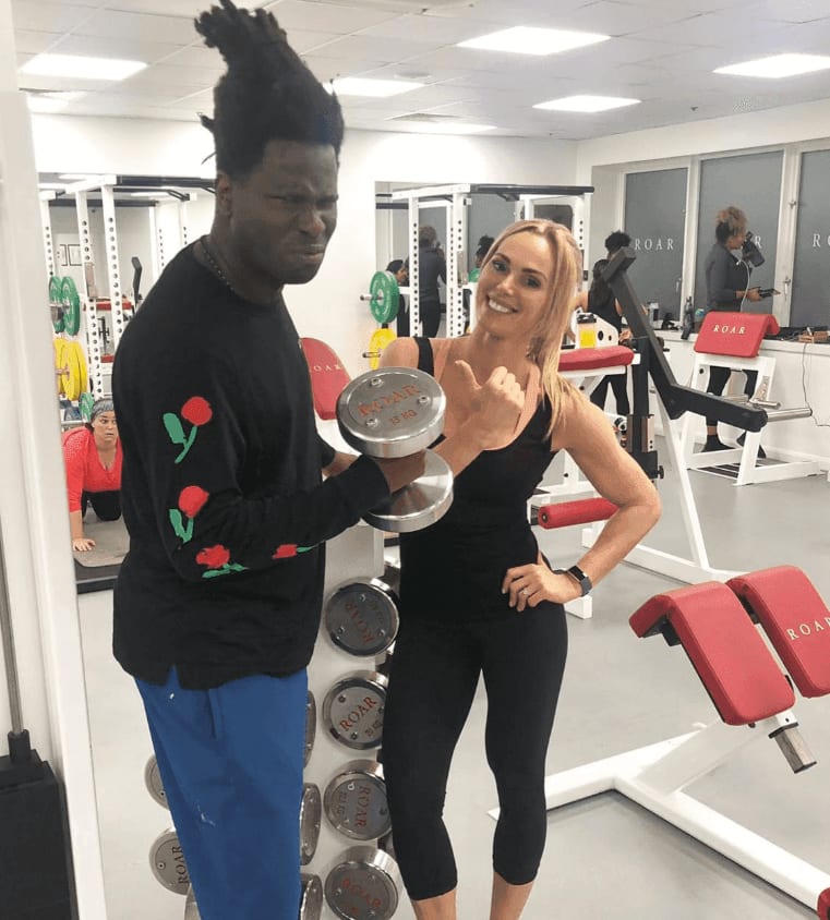 Bradley Theodore holding a dumbbell beside a ROAR trainer flexing her arm at ROAR Fitness