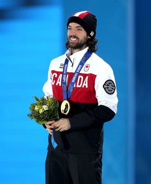 Short track speed skater Charles Hamlin holding flowers and a gold medal in a Canada jacket at Sochi 2014