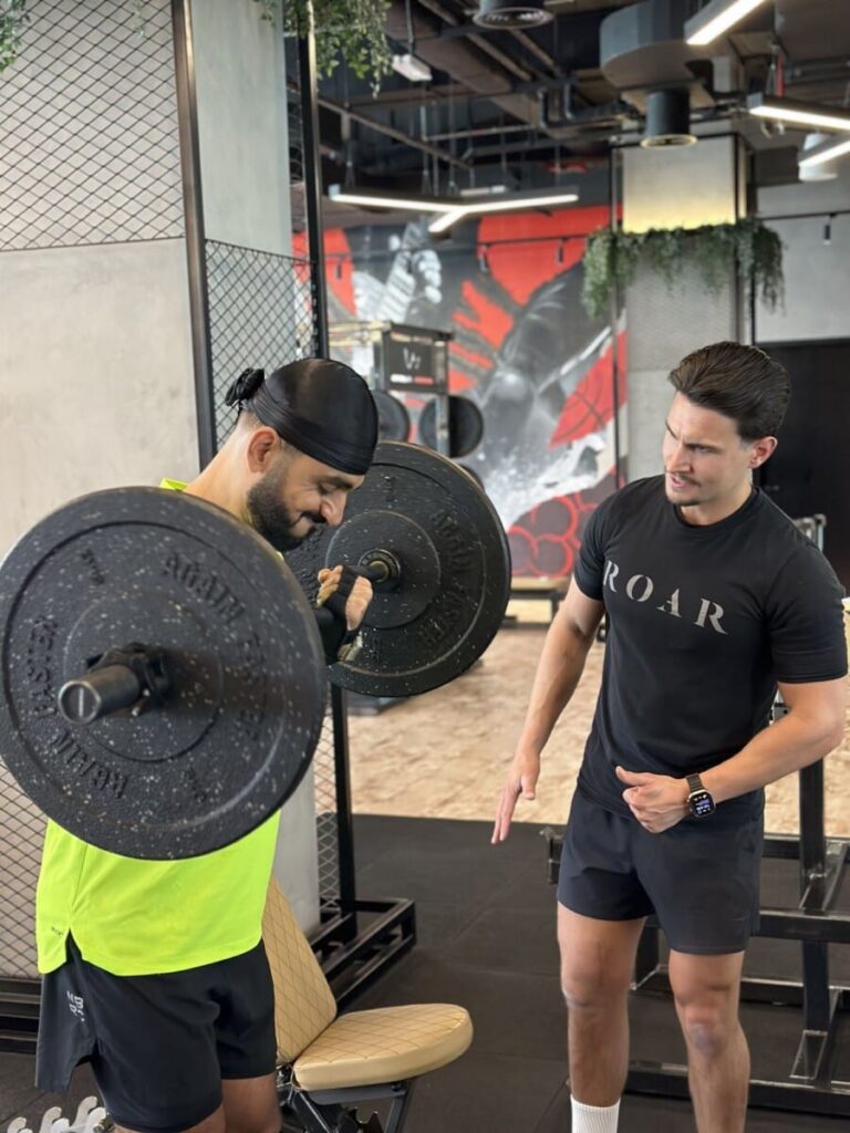 DJ Bliss lifting a barbell while a ROAR personal trainer gives instructions at ROAR Fitness Dubai