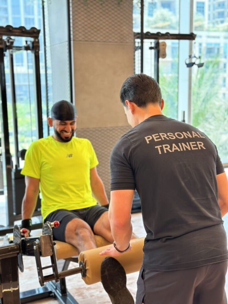 DJ Bliss on the leg extension machine facing a ROAR personal trainer at ROAR Fitness Dubai