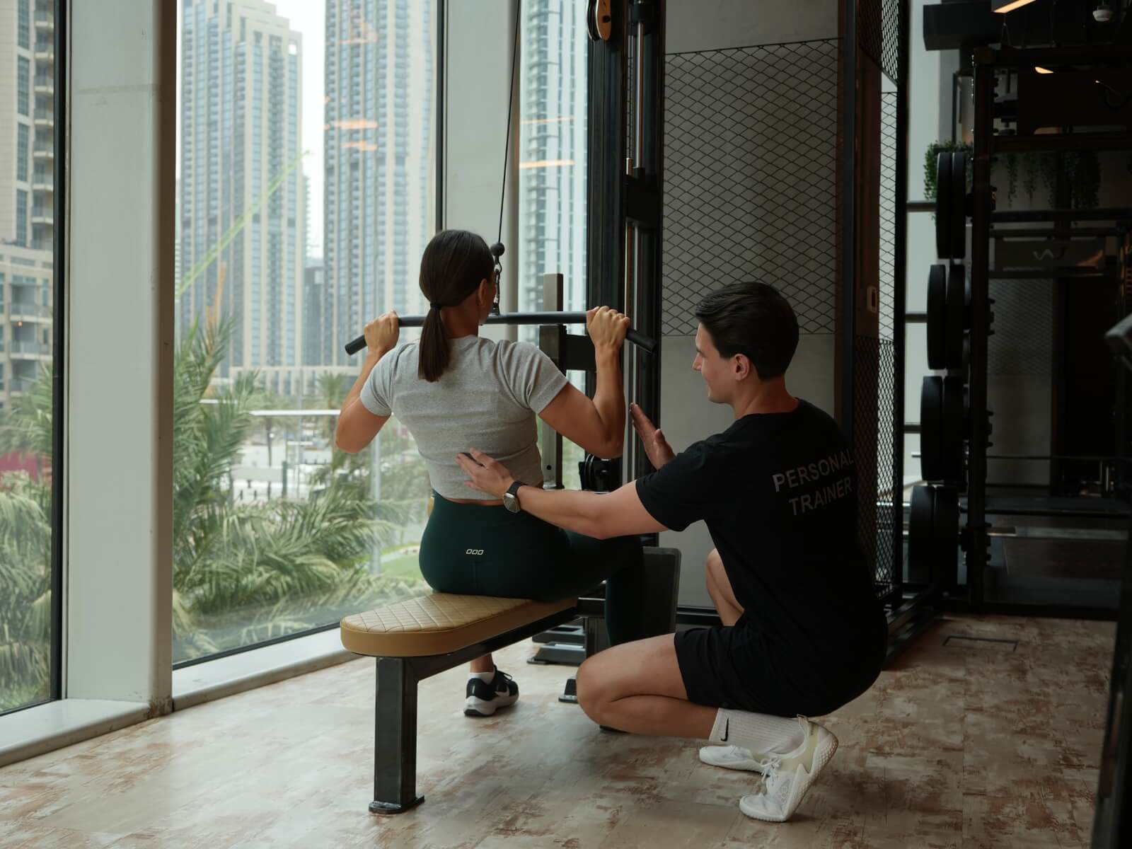 Personal trainer correcting lat pulldown form at Roar Fitness Dubai, overlooking Downtown Dubai