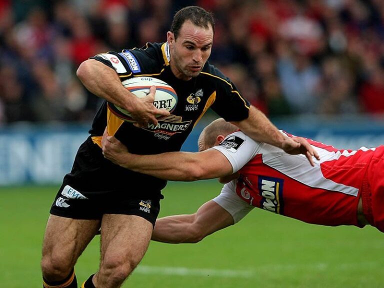 Rugby player Mark Robinson running with the ball as an opponent dives to tackle him