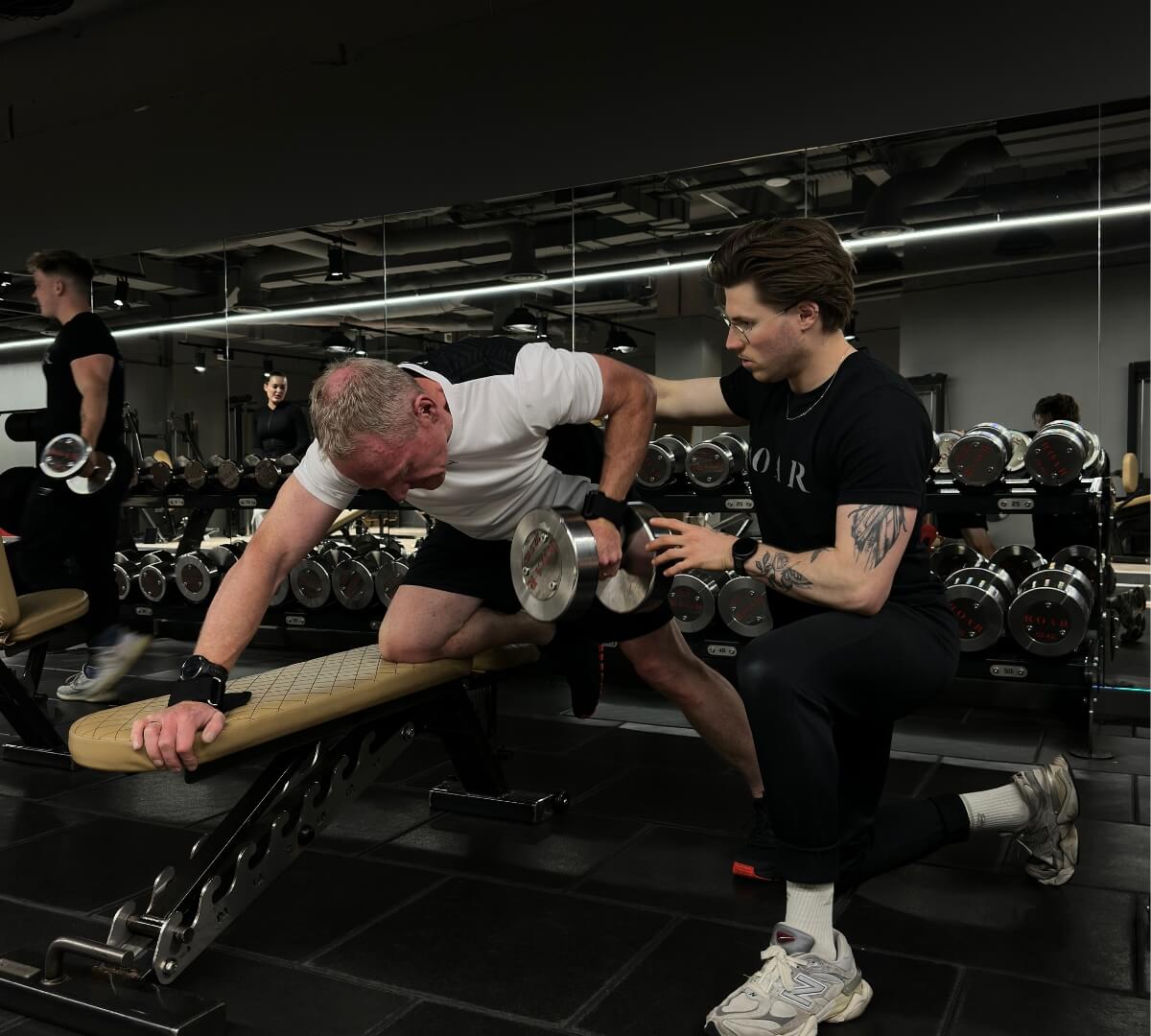 ROAR Fitness personal trainer supporting a client's dumbbell row form as part of a muscle building programme