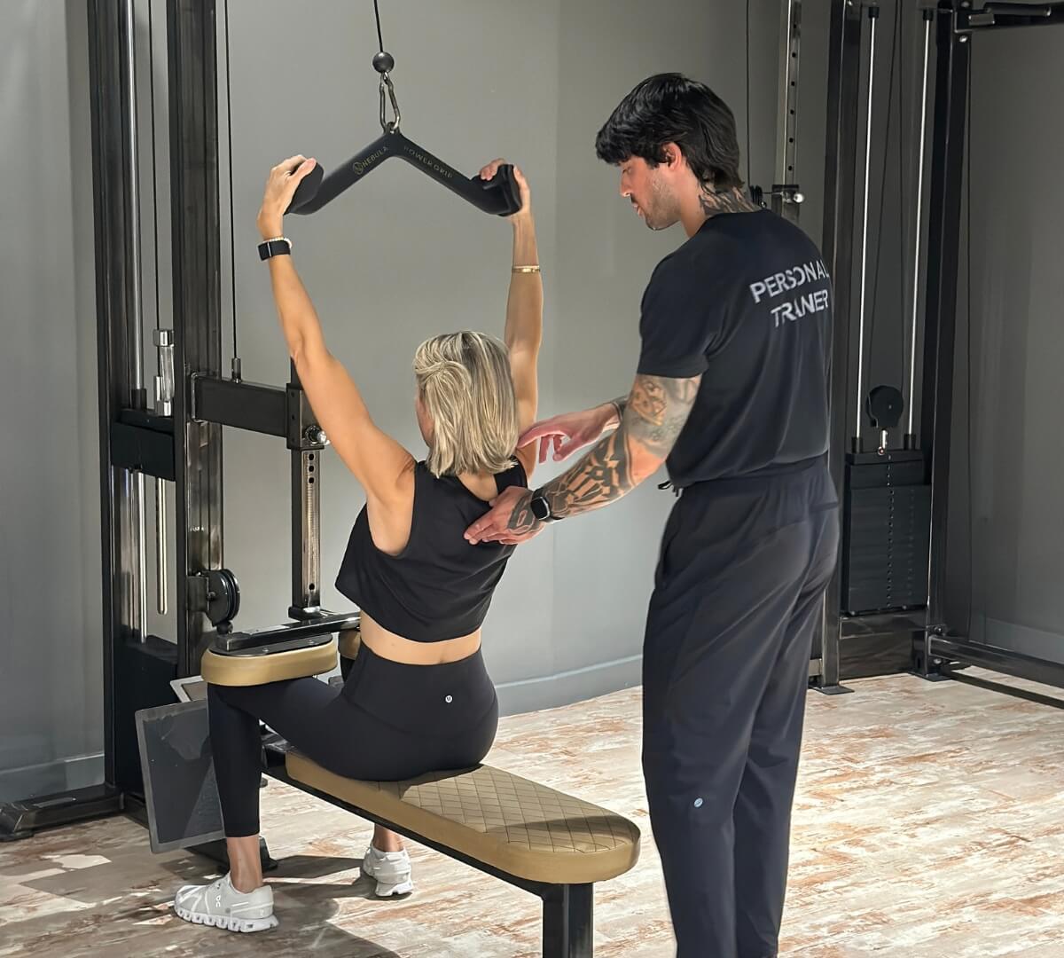 Woman performing a seated lat pulldown with a Roar Fitness personal trainer correcting her back and shoulder form
